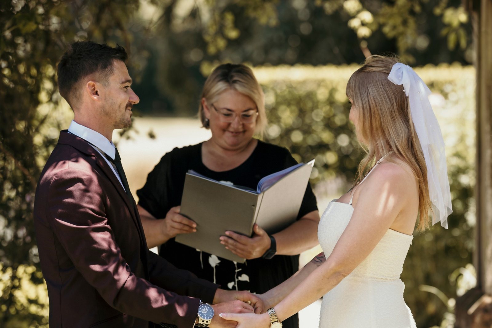 Danielle smiling as she reads from her ceremony folder, with a couple holding hands in front of her